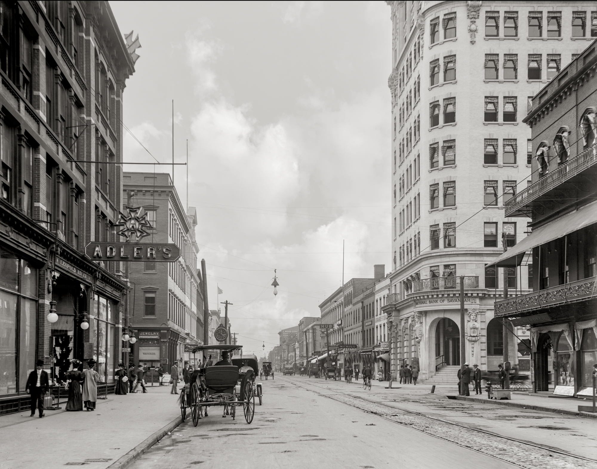 Camera is at eye level looking down Broughton Street to the West. There are signs for banks and stores with a horse drawn buggy in the foreground.