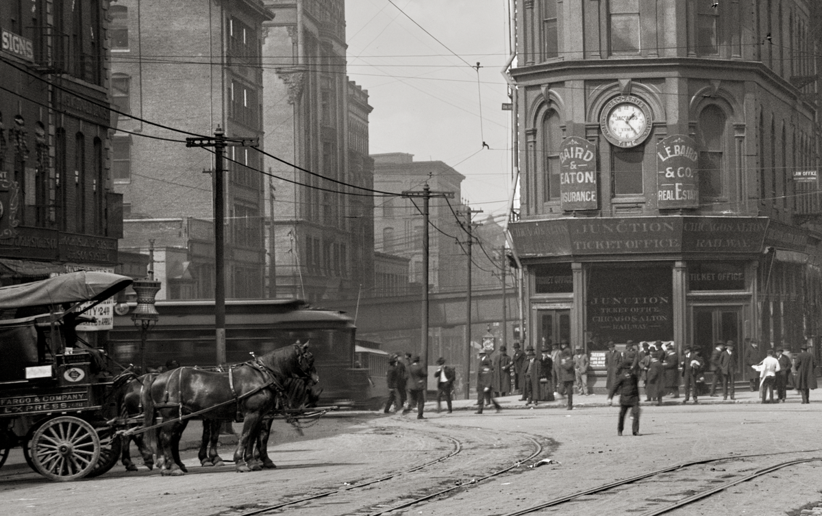 Closeup of buggy with horses and people walking in the street with trolley car tracks.