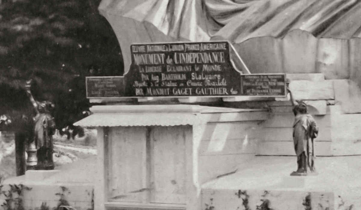 The closeup of a sign below the head of the Statue of Liberty.