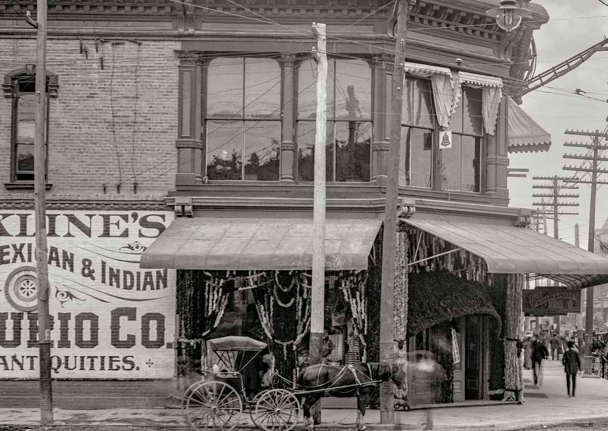 Side view of a horse and carriage parked outside a Mexican &amp; India Curio Co. Antiques on El Paso Street.
