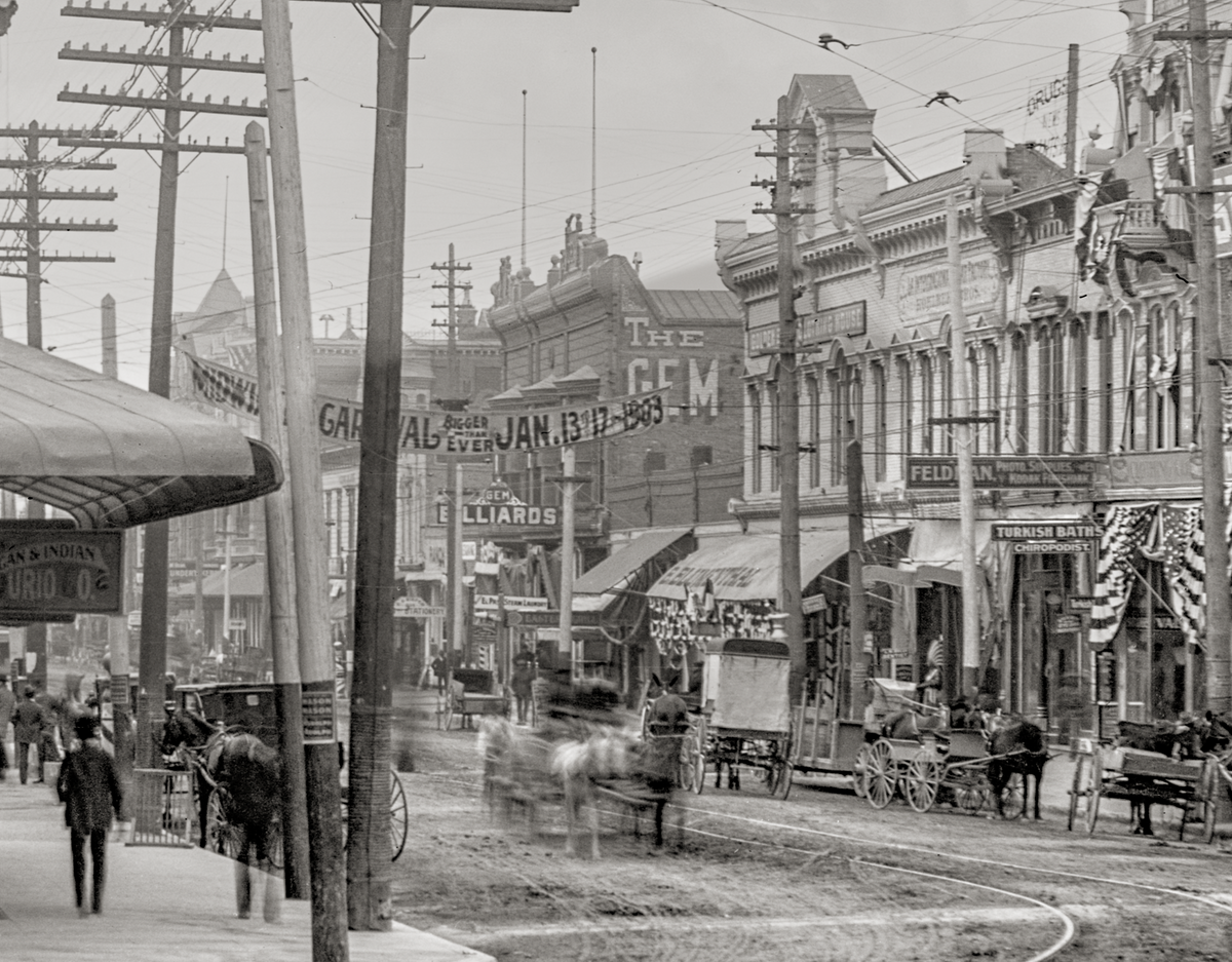 Closeup of horses in street with a banner of the street  of a carnival on January 13-17, 1903.