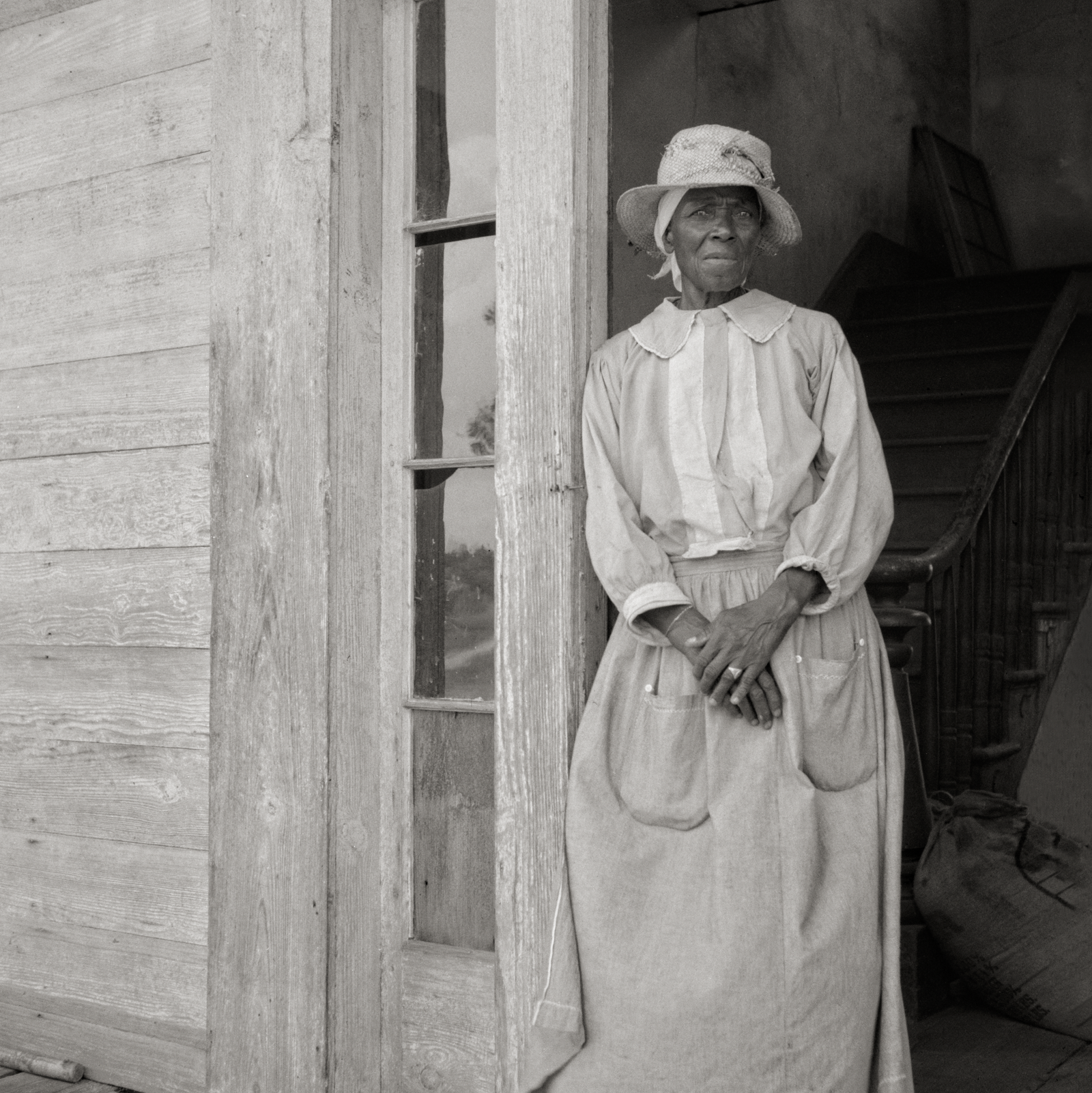 Black Woman standing in doorway with hands clasped.