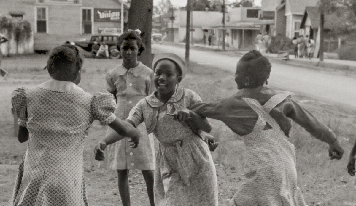 A closeup of a girl, smiling, with another girl in back of her looking straight into the camera.